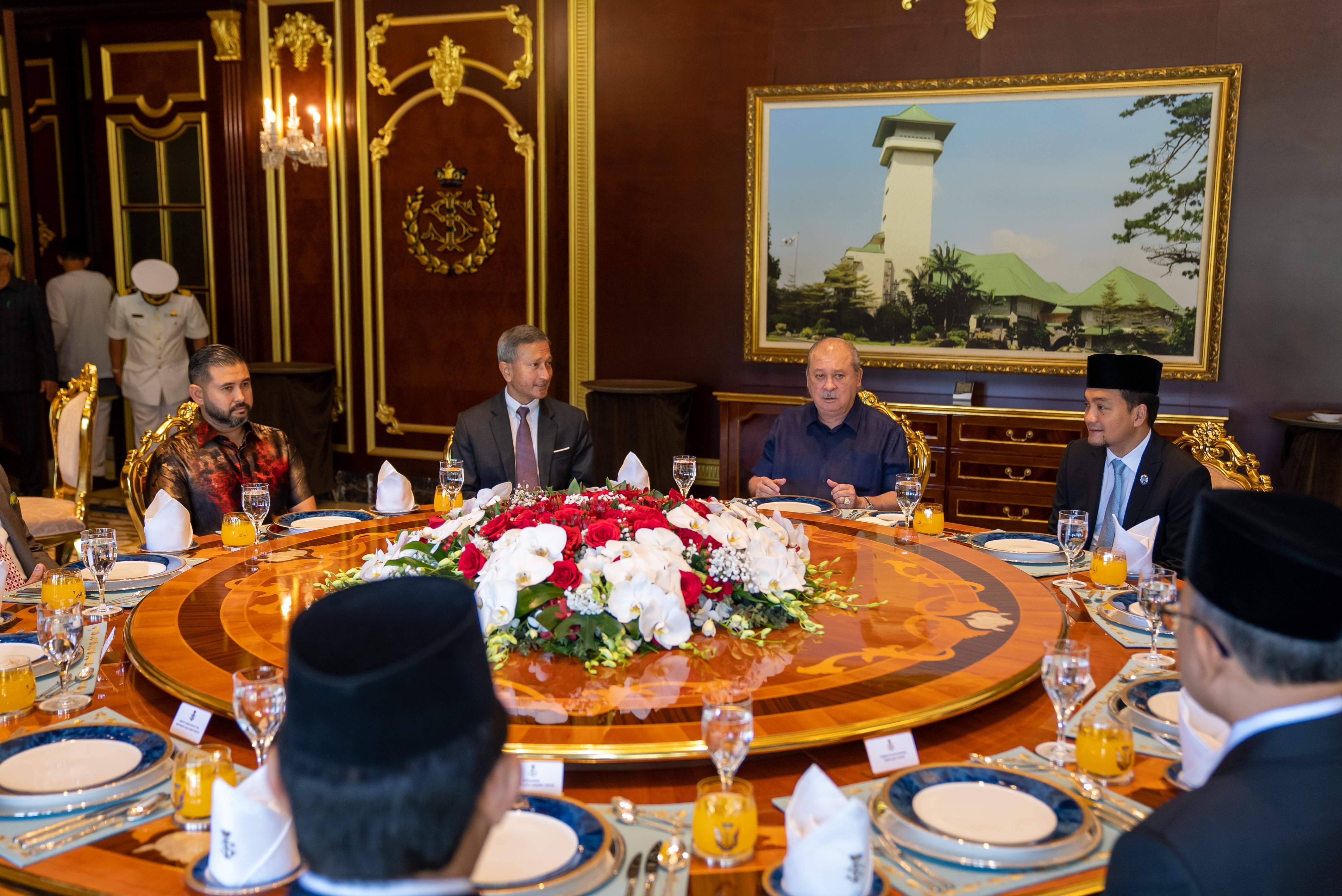 People seated at a round table laden with floral arrangements and place settings.
